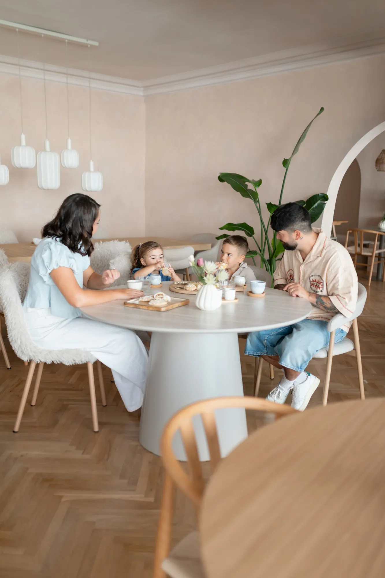 Eine Familie sitzt zu viert an einem runden Tisch im hellen Gastraum und trinkt gemeinsam.