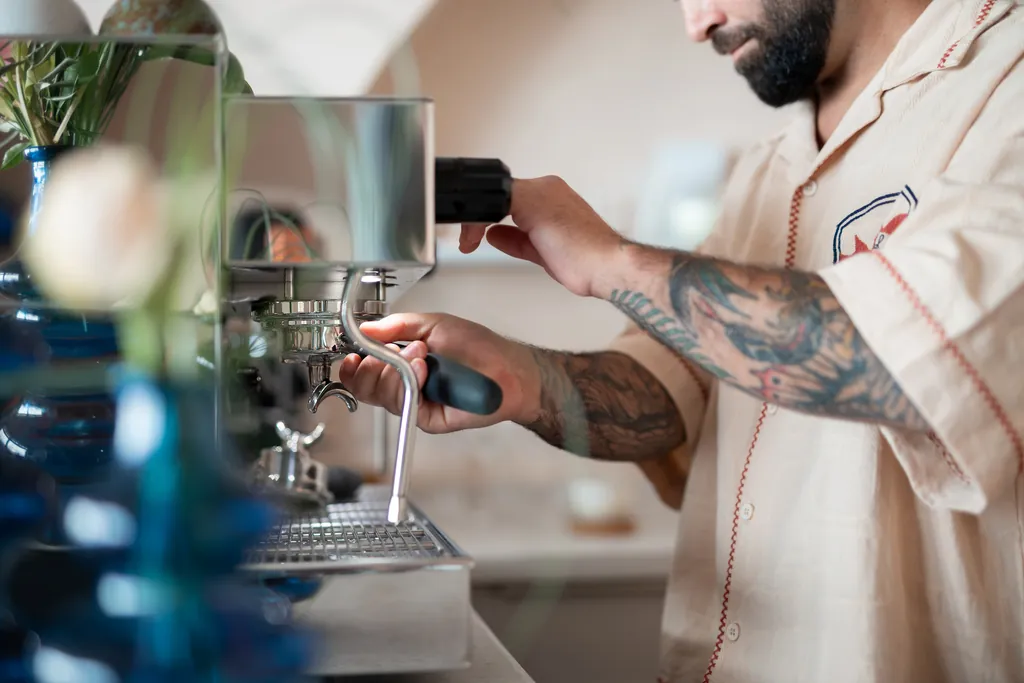 Hände an der Siebträger-Espressomaschine, im Vordergrund unscharfe blaue Glasvasen